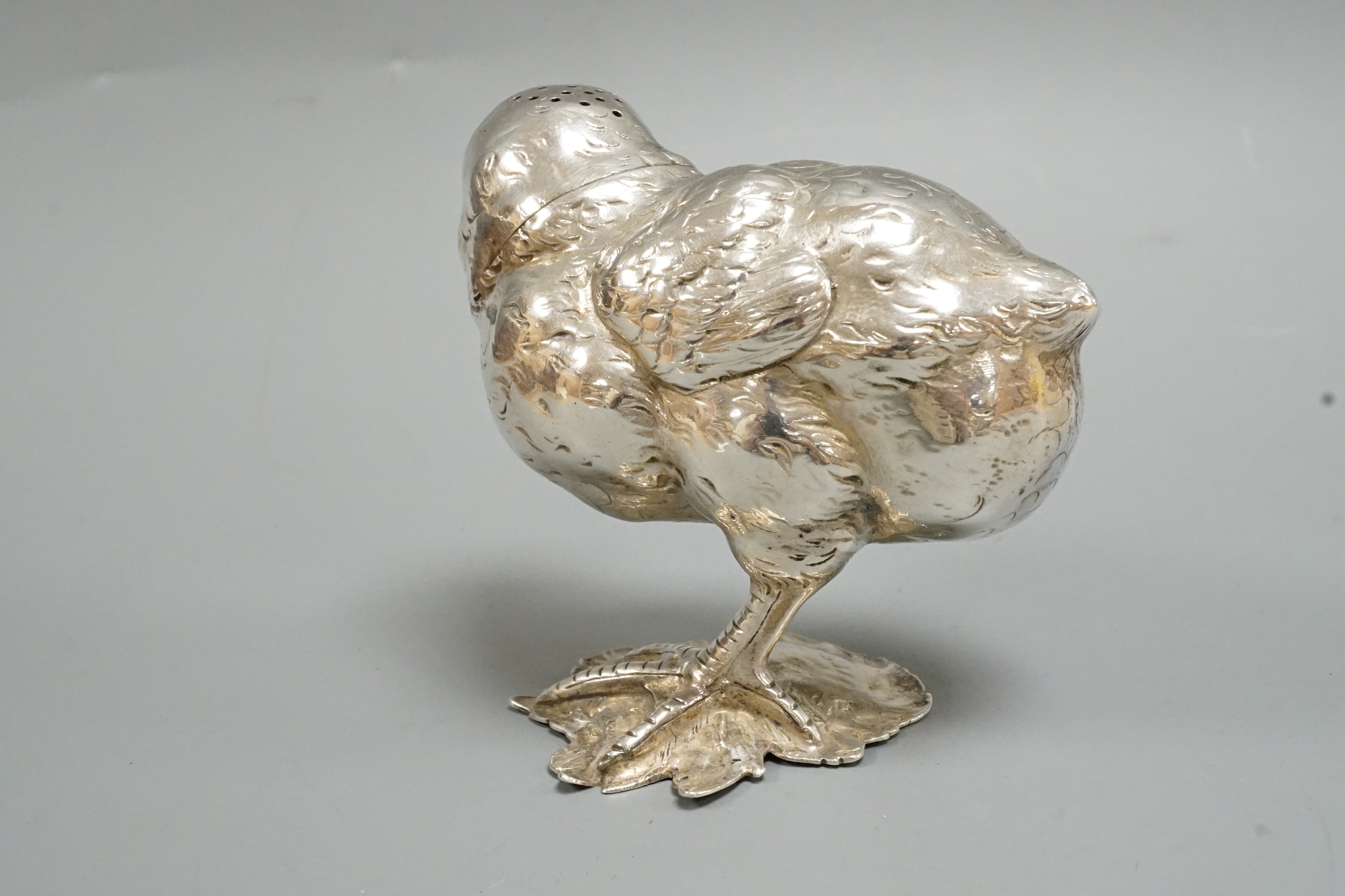 A novelty white metal pepperette, modelled as a chick on one leg, scratching, height 89mm.